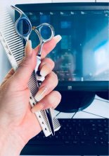 Hand holding a scissor and comb in front of a computer at the klink salon London